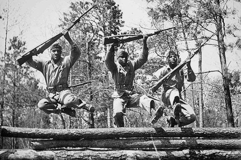 Three Marines jump over logs with their rifles.