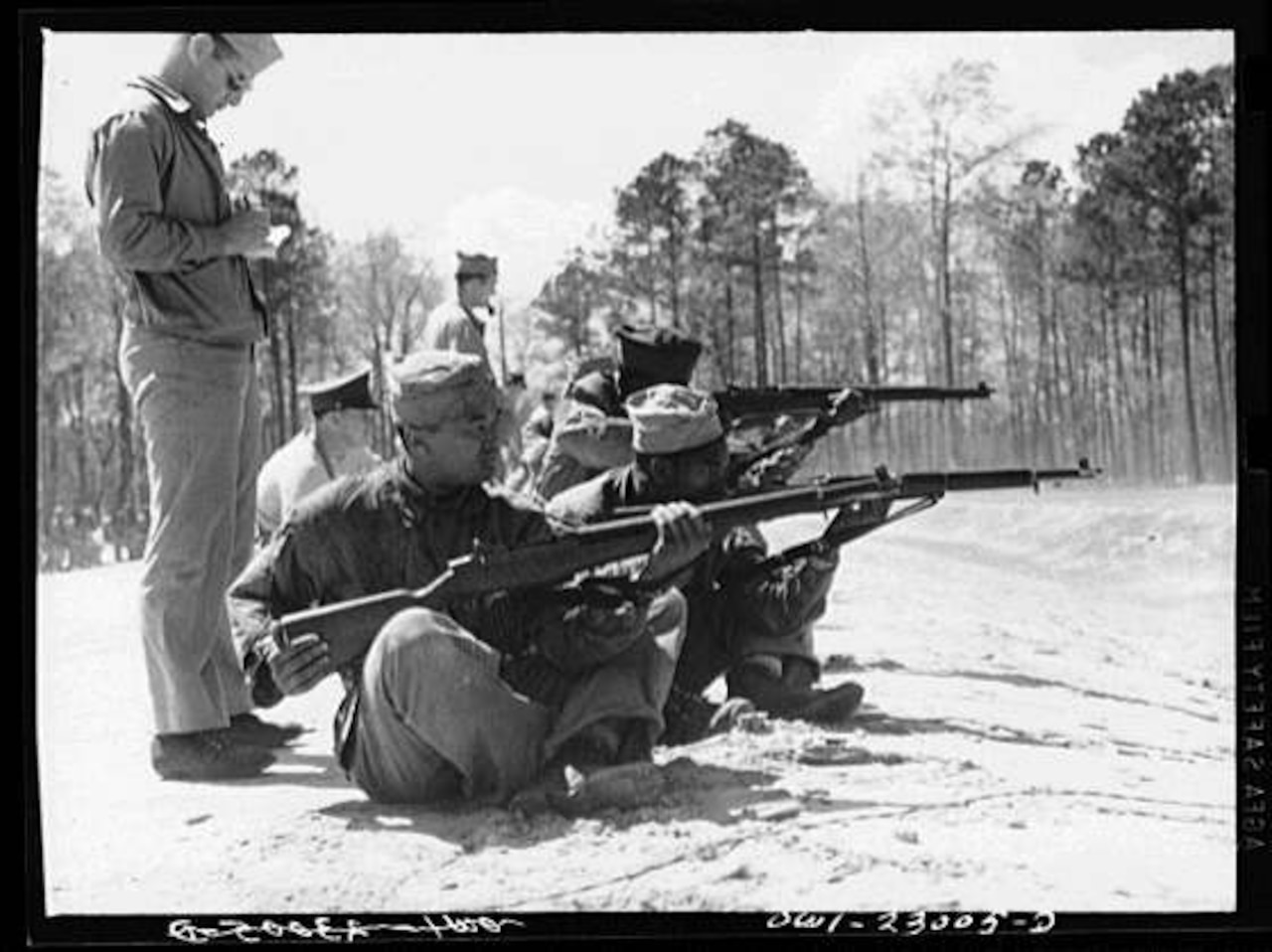 Marines train by firing their rifles downrange as a man take notes.