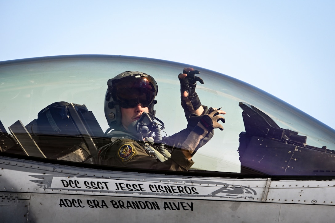 A pilot makes a hand signal from inside a cockpit.