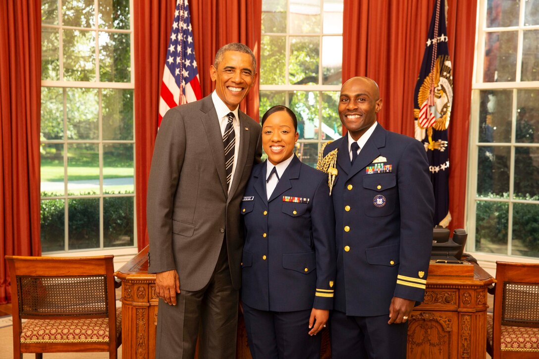 Two military personnel stand next to president Obama in the Oval Office.
