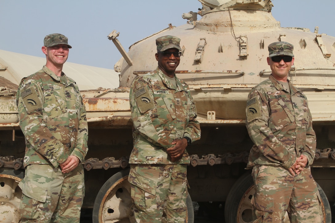 Three smiling soldiers stand in front of tactical vehicle and pose for a photo.