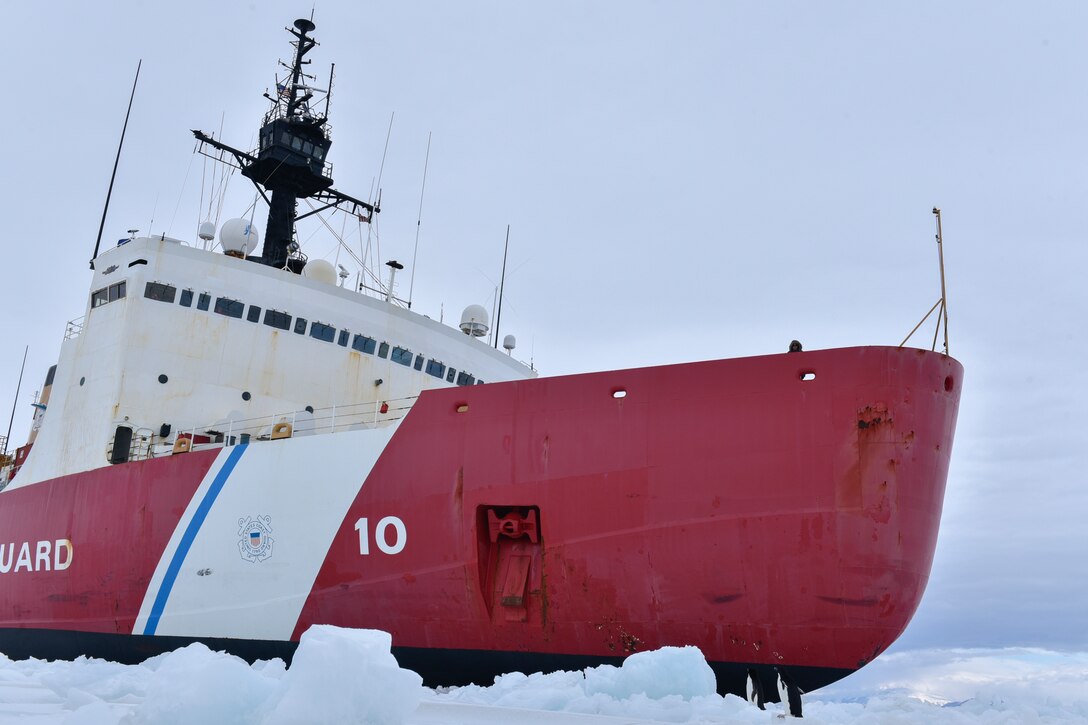 A large ship is surrounded by ice. At the front end, two penguins stand near it.