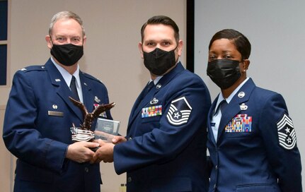 Col. Terry McClain, 433rd Airlift Wing commander, and Chief Master Sgt. Takesha Williams, 433rd AW command chief, present the Senior Noncommissioned Officer of the Year award to Master Sgt. Justin Lundgaard, 26th Aerial Port Squadron, at the wing’s annual awards ceremony Feb. 5, 2022, at Joint Base San Antonio-Lackland, Texas. (U.S. Air Force photo by Staff Sgt. Monet Villacorte)