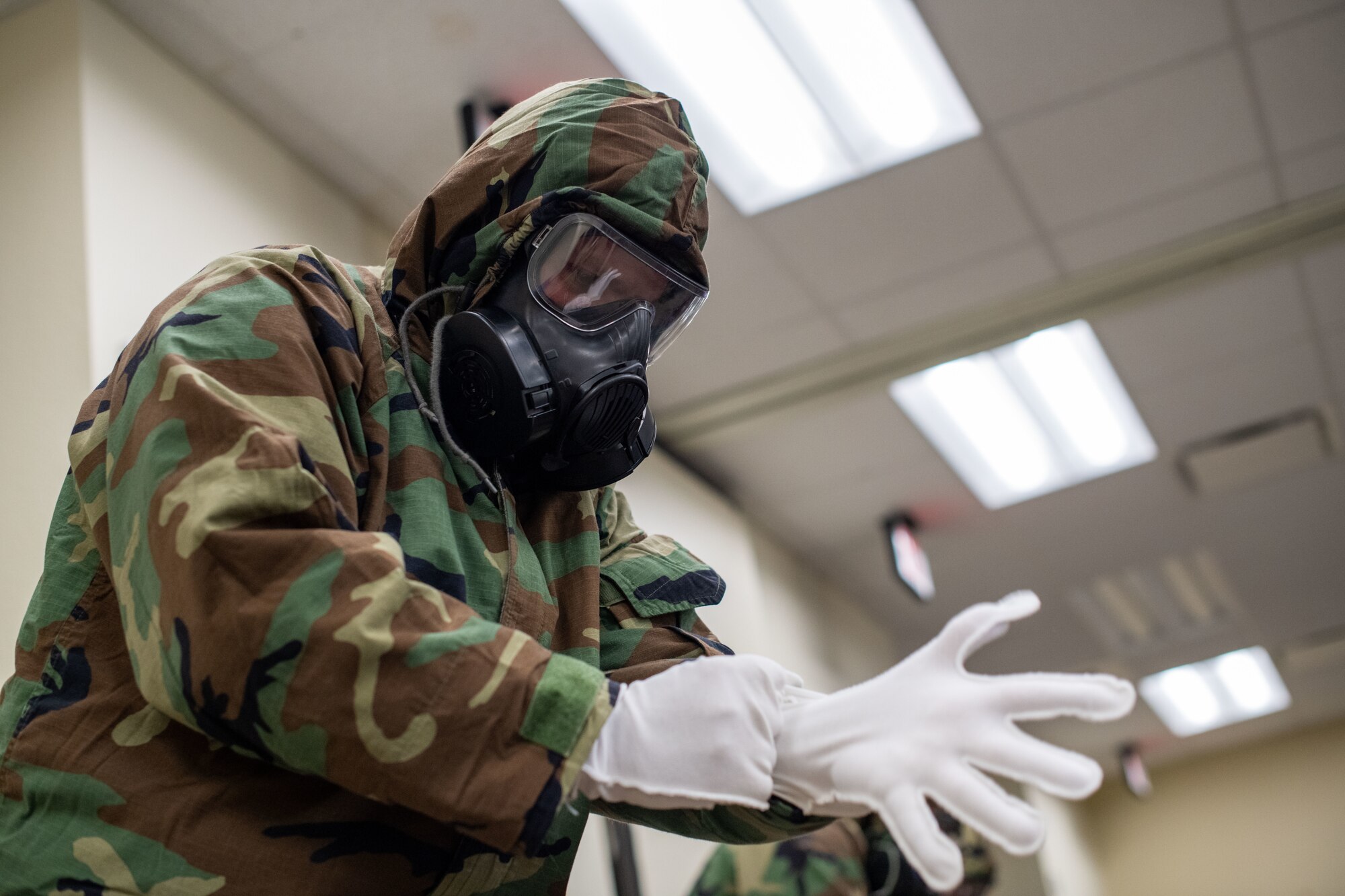 An Airmen in full chemical protective gear puts on a white glove