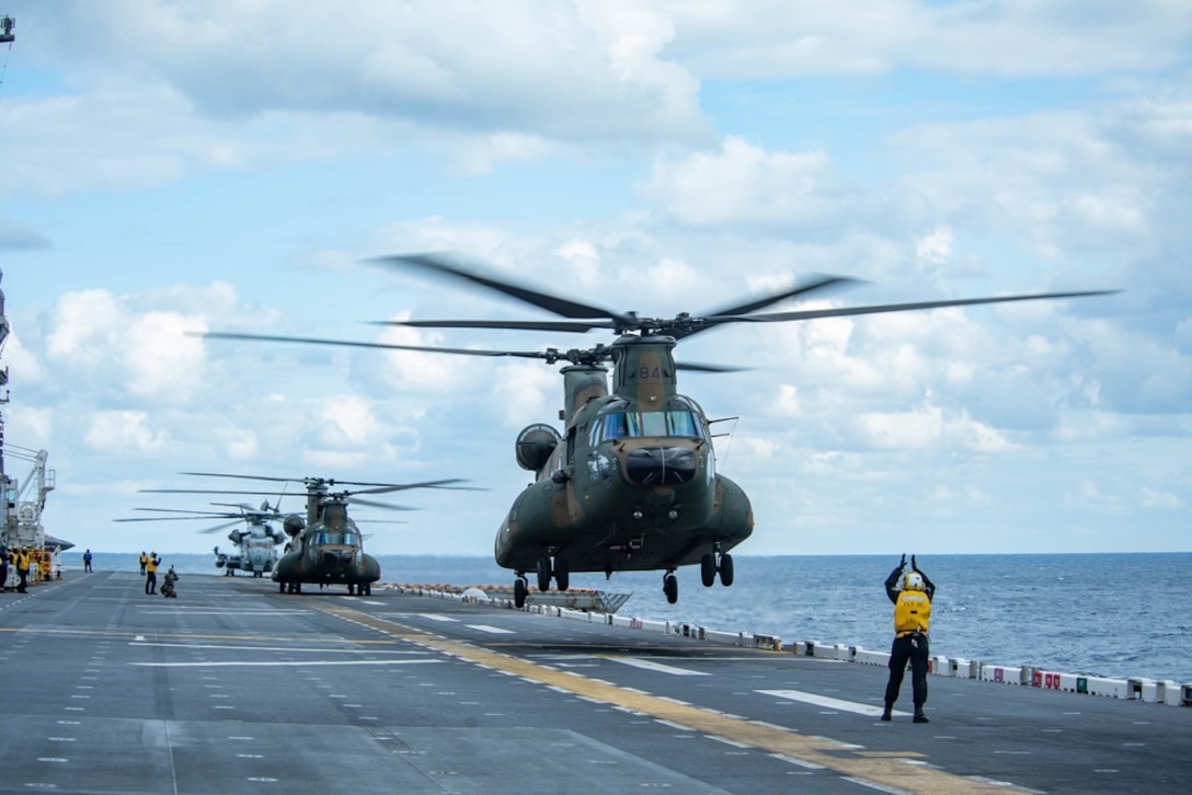 PHILIPPINE SEA (Feb. 6, 2022) Aviation Boatswain’s Mate (Handling) 3rd Class Shelby Mann, from Udall, Kan., assigned to the forward-deployed amphibious assault ship USS America (LHA 6), signals a CH-47J Chinook helicopter from the Japan Ground Self-Defense Force to take off from the ship’s flight deck during Exercise Noble Fusion. Noble Fusion demonstrates that Navy and Marine Corps forward-deployed stand-in naval expeditionary forces can rapidly aggregate Marine Expeditionary Unit/Amphibious Ready Group teams at sea, along with a carrier strike group, as well as other joint force elements and allies, in order to conduct lethal sea-denial operations, seize key maritime terrain, guarantee freedom of movement, and create advantage for U.S., partner and allied forces. Naval Expeditionary forces conduct training throughout the year, in the Indo-Pacific, to maintain readiness. (U.S. Navy photo by Mass Communication Specialist 2nd Class Vincent E. Zline)