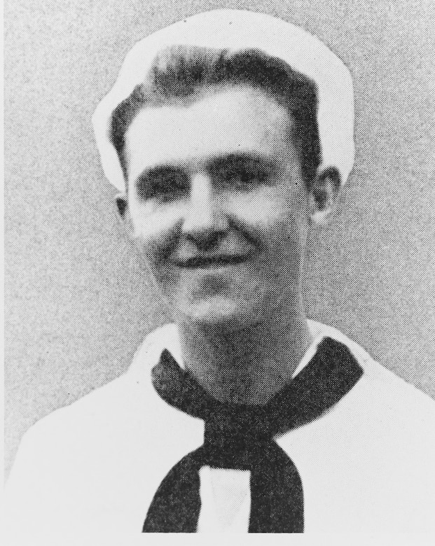 A young sailor in dress white uniform smiles for the camera.