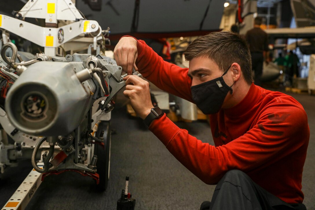 A sailor wearing a mask performs maintenance on a ship.