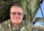 Head and shoulders image of a man wearing camo uniform with patches outdoors.