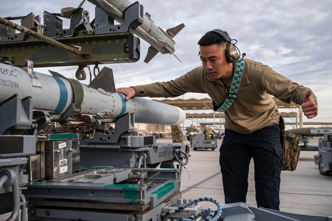 An airman bends forward and holds a missile.