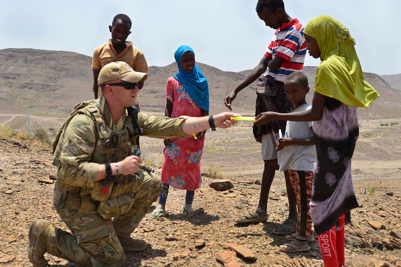 A service member hands something to a child as four other children watch.
