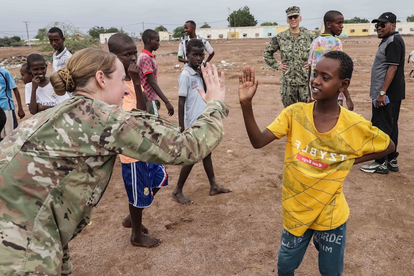 A female soldier gives a high-five to a child as other children watch.