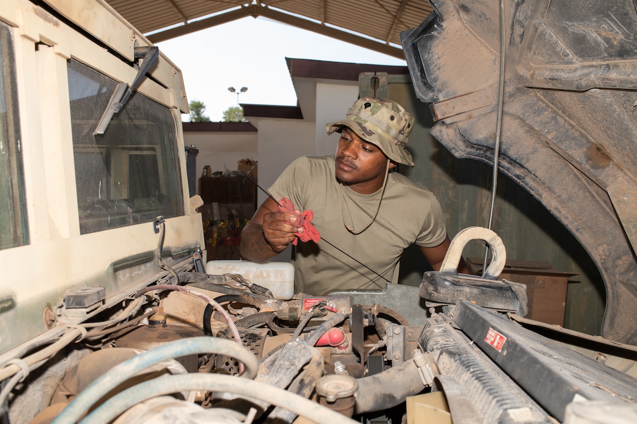 A male service member checks the oil gauge in a vehicle.