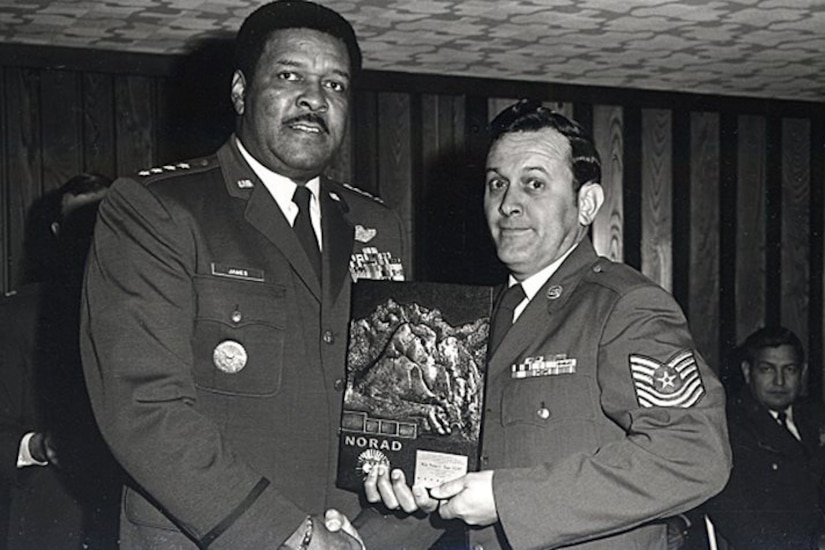 Two men shake hands while also holding a small plaque.