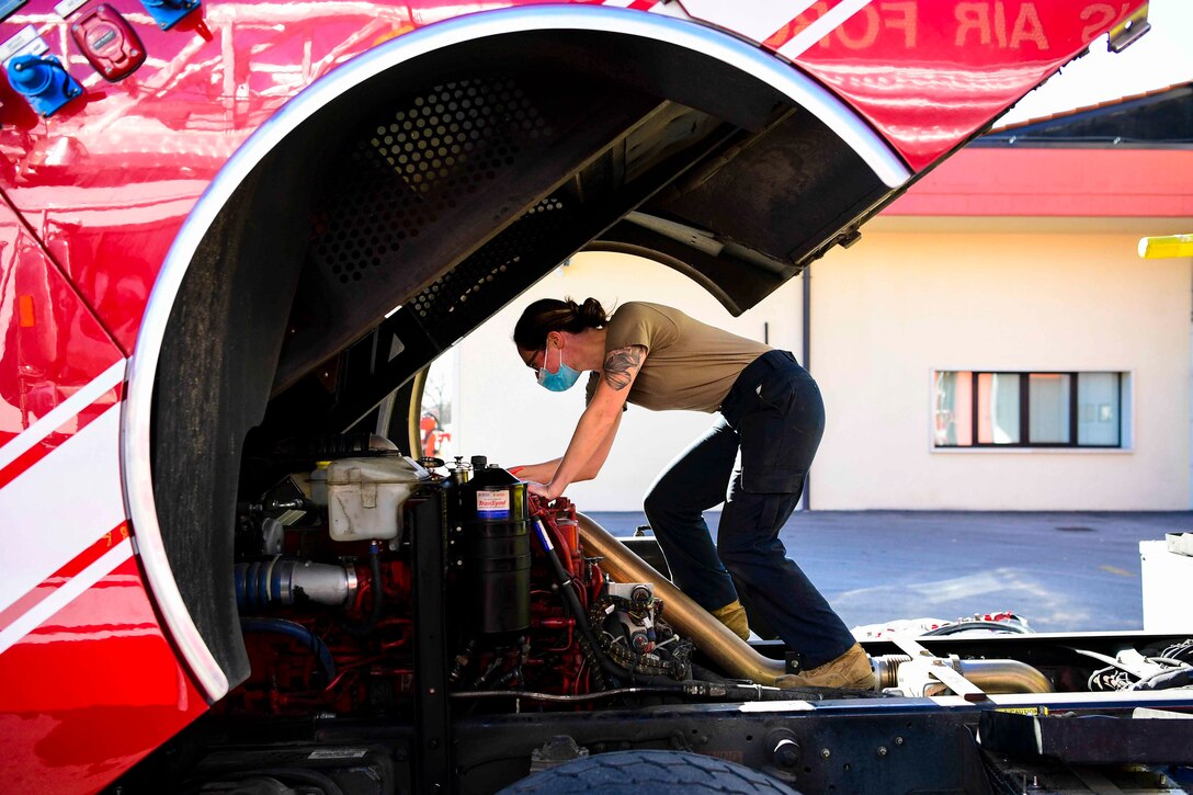 An airman works on a firetruck engine.