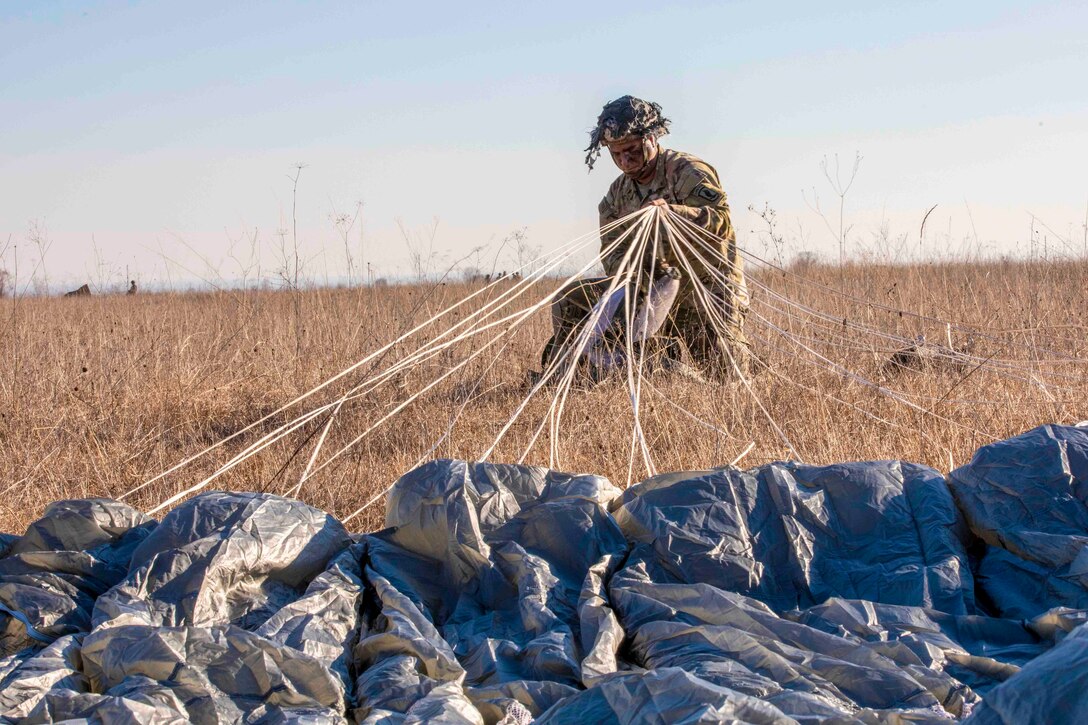 A soldier pulls on strings from a parachute.