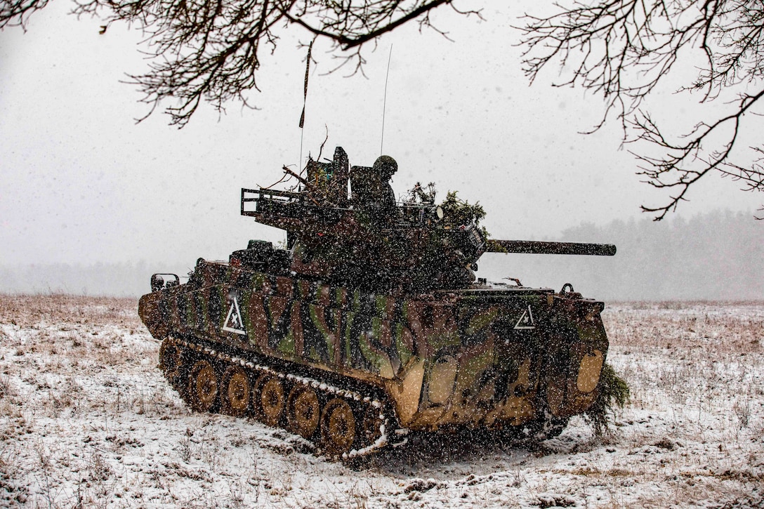 Soldiers travel in a tank through a snowy area.