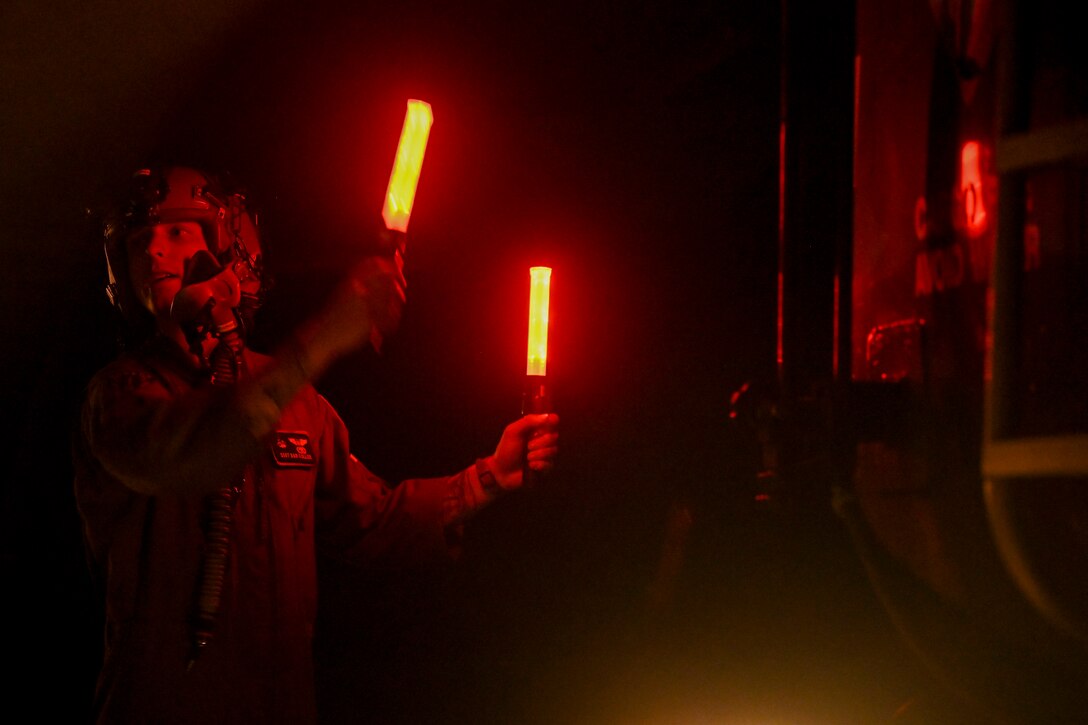 An airman uses red lights to guide a truck at night.