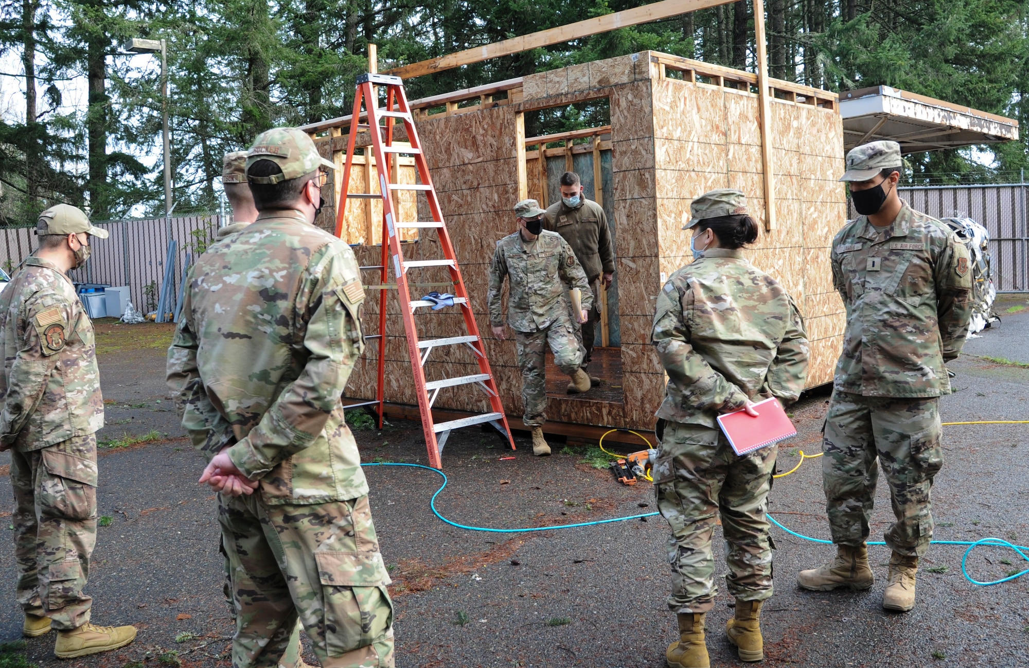 Airmen look at a training project made of wood to help airmen hone their civil engineering skills.