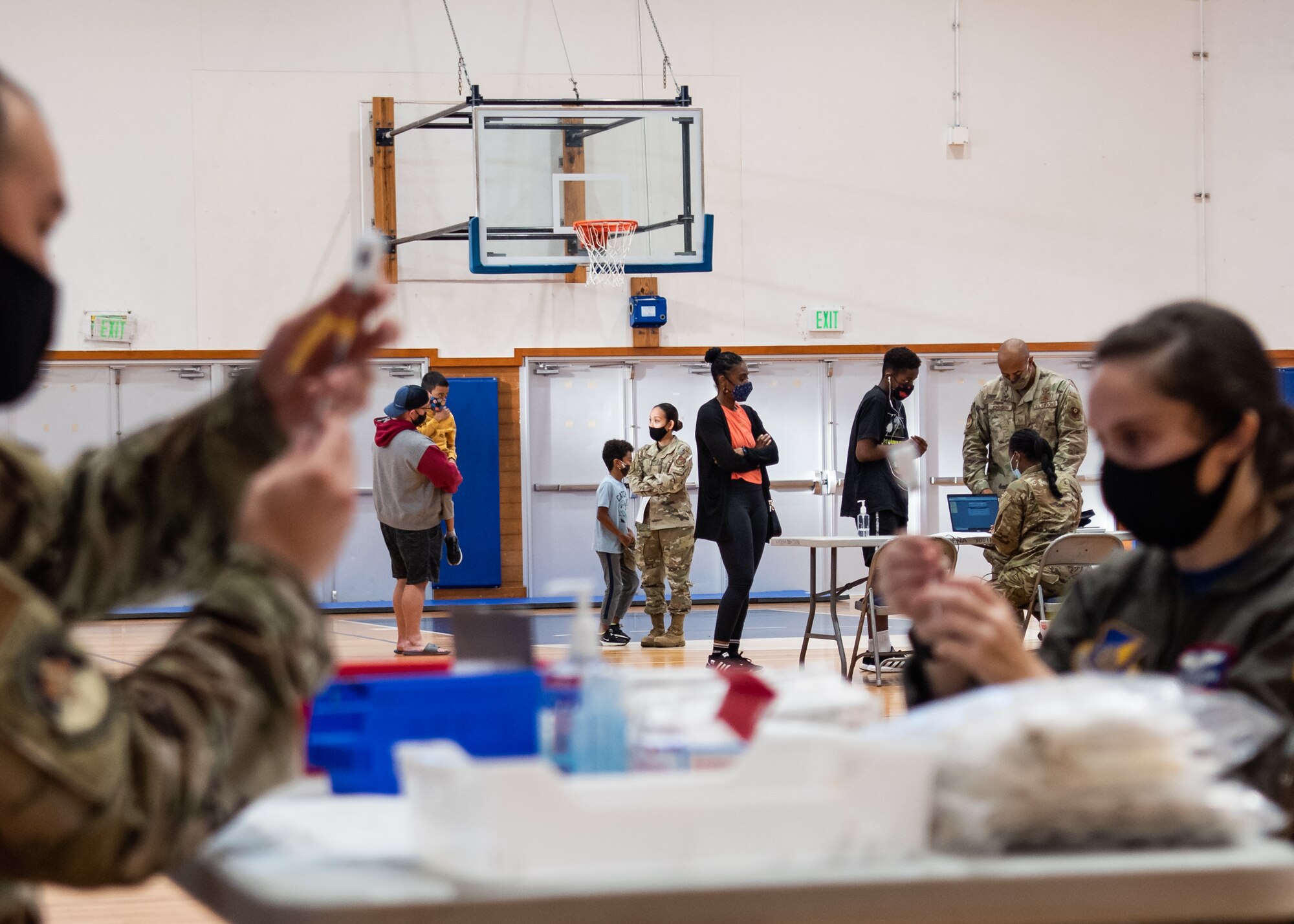 Two Airmen draw syringes while people line up in the background.