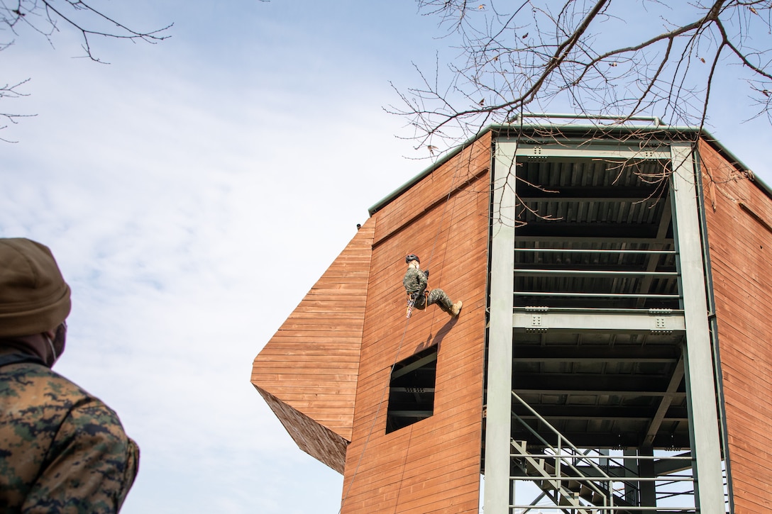 A Marine watches as another rappels down the side of a building.