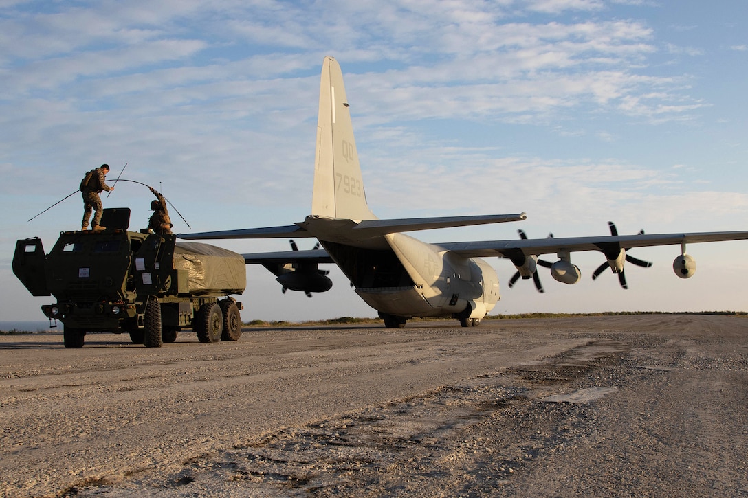 Two Marines set up a rocket system on a vehicle behind an aircraft.