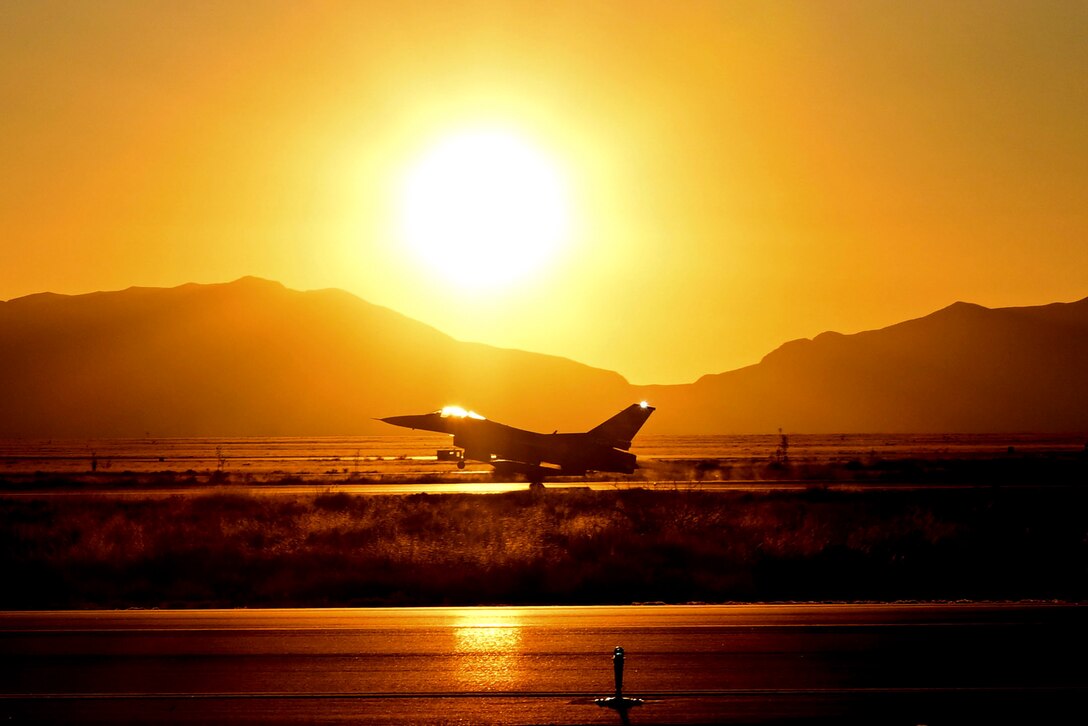 An aircraft lands on a tarmac with mountains in the background under a sunlit sky.