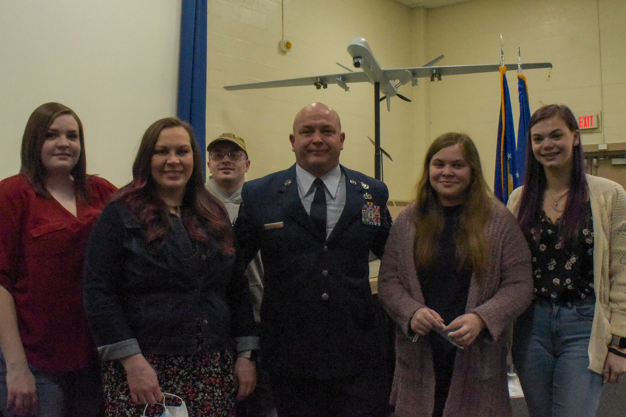 A man in Air Force dress blue uniform poses for a photo with his family; his wife, three young women and a young man.