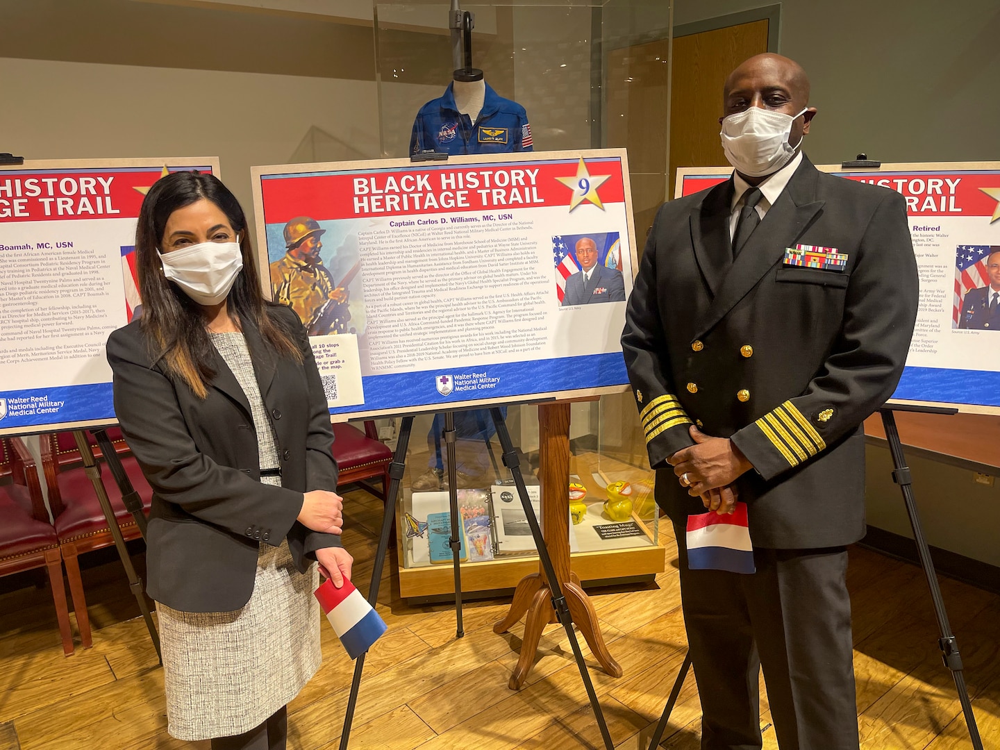 Ms. Maia Magder (L) and Captain Carlos D. Williams, MC, USN (R) stand next to the poster telling CAPT Williams' story at the Ribbon Cutting Ceremony at Walter Reed National Military Medical Center (WRNMMC) for the 2022 Black History Heritage Trail.