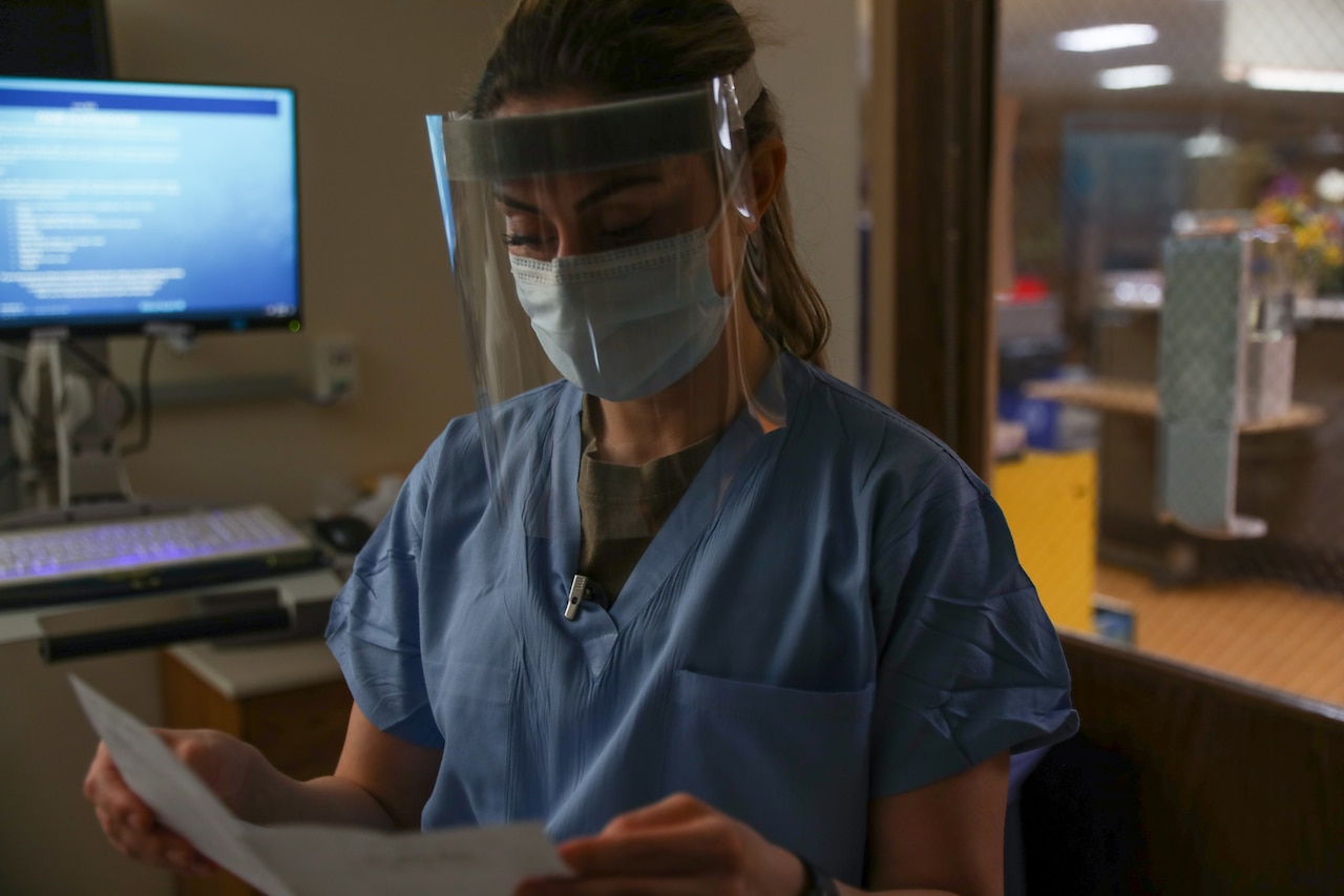 A woman wearing personal protective equipment reads a sheet of paper.