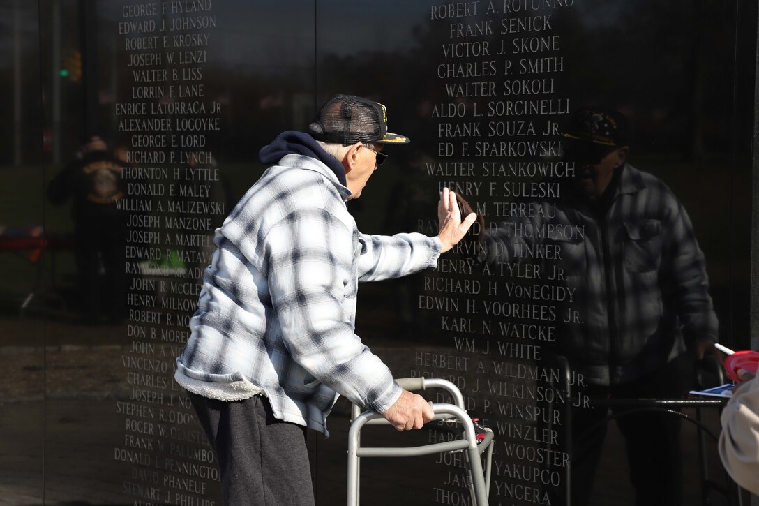 A veteran places his hand on the names etched into a memorial wall.