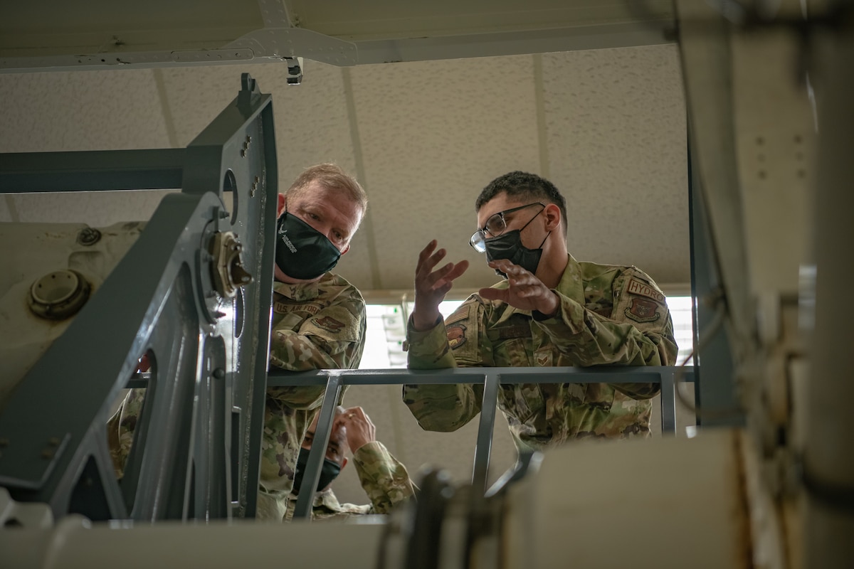 Senior Airman Jordan Hughes, 349th Maintenance Squadron, briefs Lt. Gen. Richard W. Scobee, chief of the Air Force Reserve and commander of the Air Force Reserve Command, on the mechanics of their landing gear training simulator at Travis Air Force Base, California, Feb. 12, 2022. Scobee and his senior enlisted advisor visited the 349th Air Mobility Wing to learn more about its people, mission, accomplishments, and innovation efforts.
