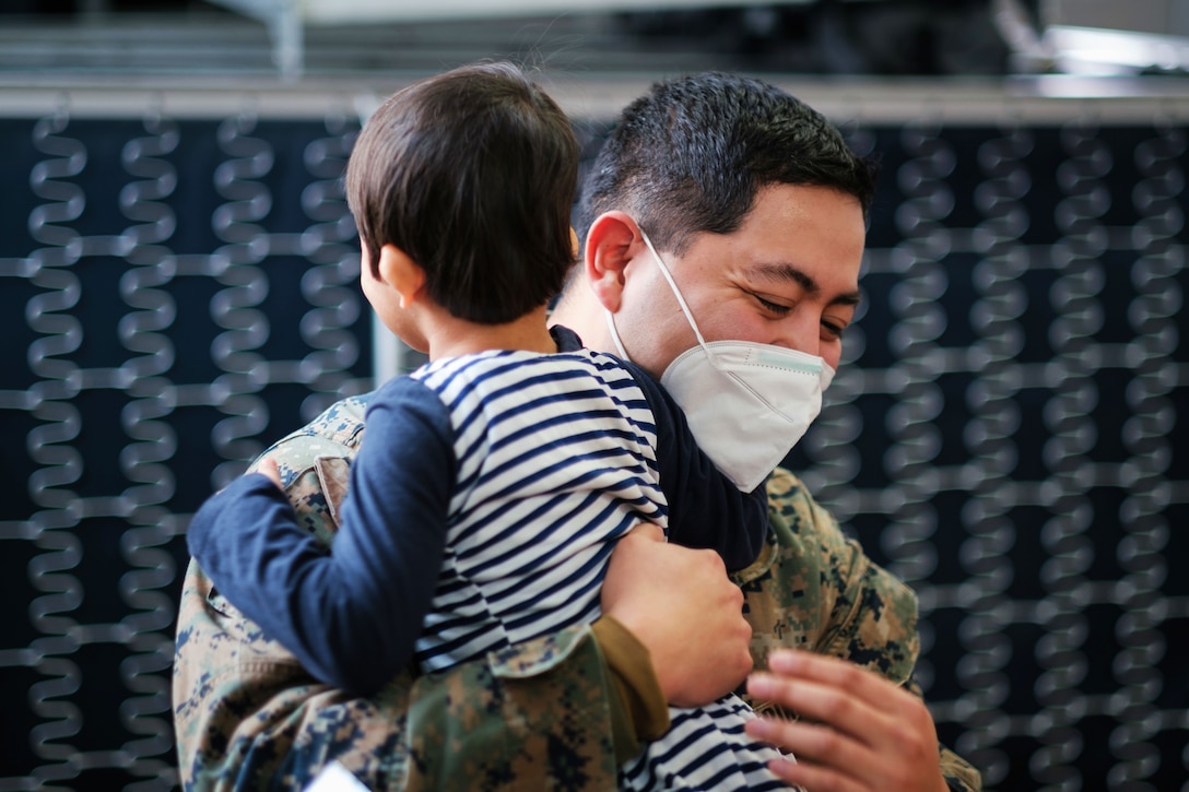 A Marine wearing a face mask smiles while hugging an Afghan child.