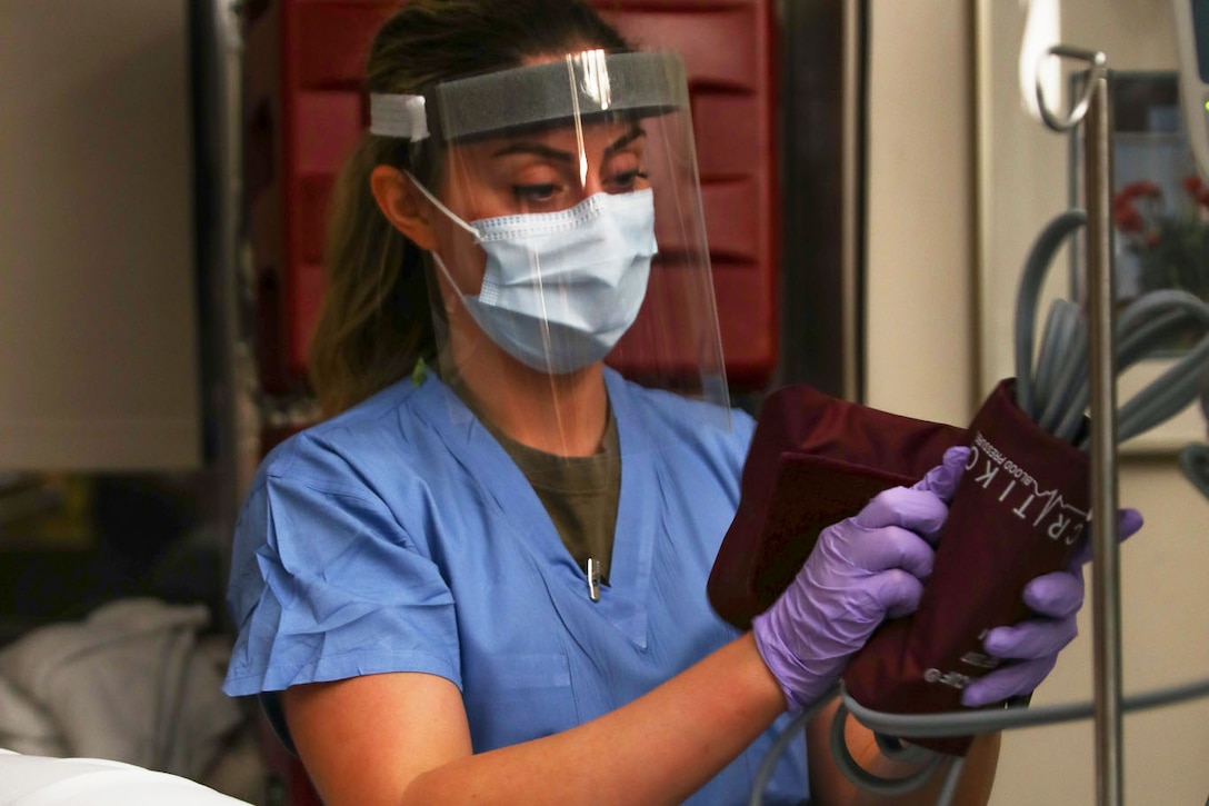 A soldier wearing a face mask unravels a blood pressure cuff.