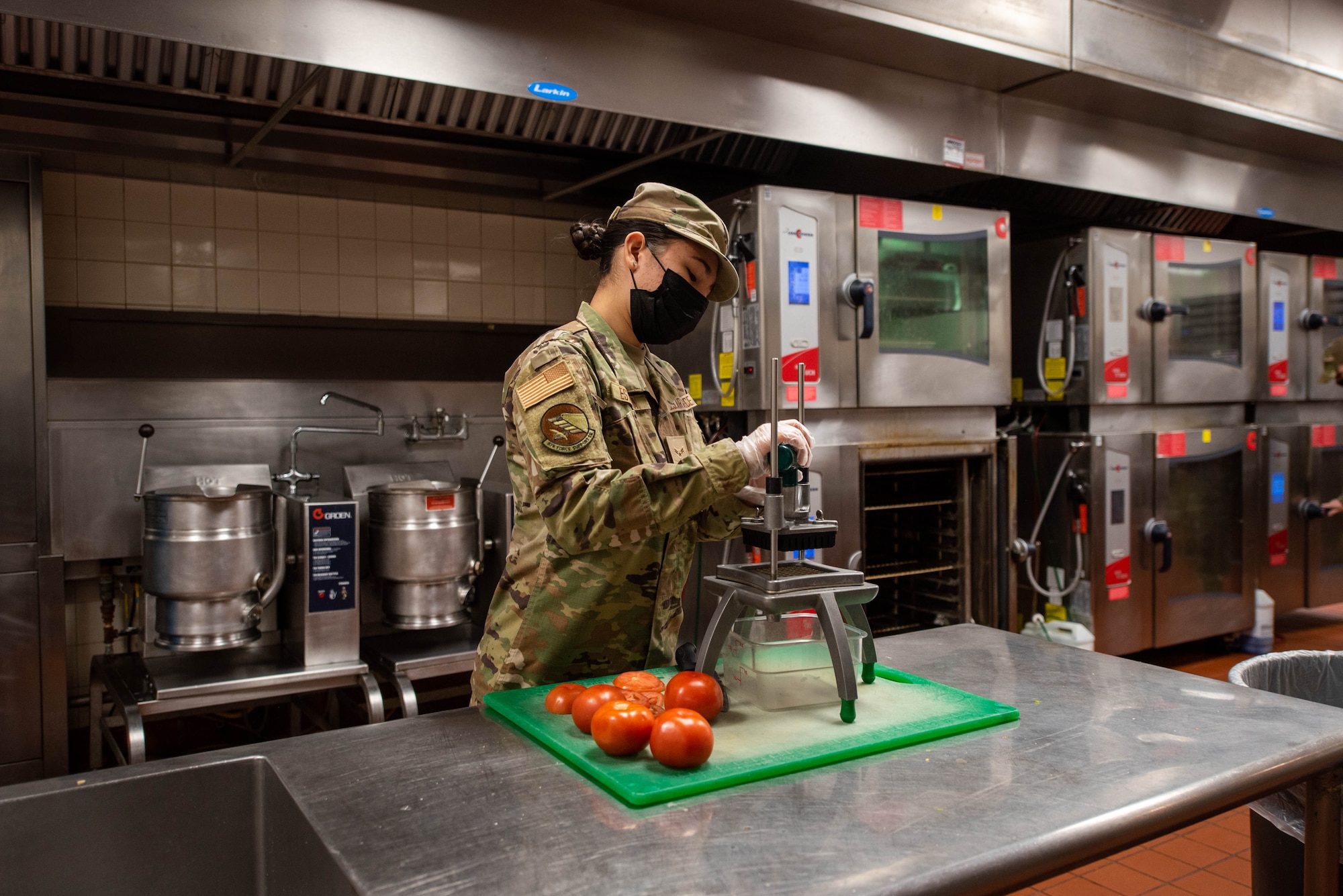Airman in kitchen chopping tomatoes.