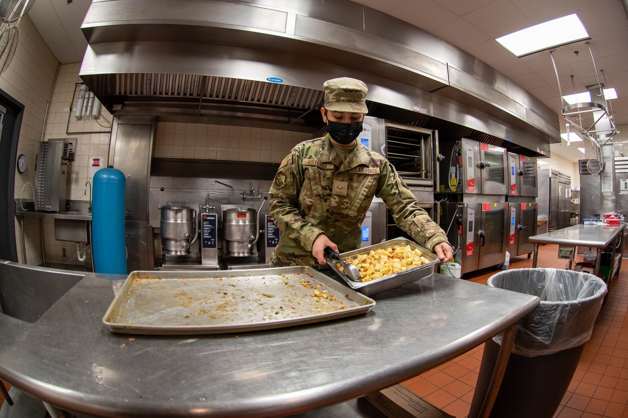 Airman in kitchen scooping potatoes.