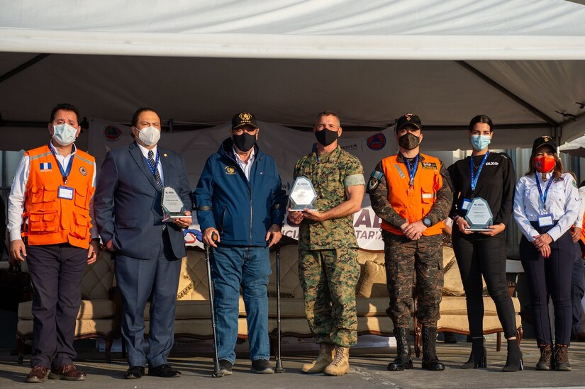 Guatemala City, Guatemala - U.S. Marine Corps Lt. Col. Jacob Reeves, the Joint Task Force-Bravo chief of staff, center, receives an award from Alejandro Eduardo Giammattei Falla, the President of Guatemala, during the closing ceremony of the Coordination Center for Natural Disaster Prevention in Central America and Dominican Republic (CEPREDENAC) II Regional Humanitarian Assistance Drill in Guatemala City, Guatemala, Feb. 4, 2022. JTF-Bravo participated in the CEPREDENAC drill through observation and an aerial firefighting exercise to build partnerships and coordination during natural disasters in the joint operating area.