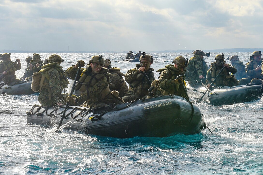 A group of Marines paddle through the water in rubber crafts.