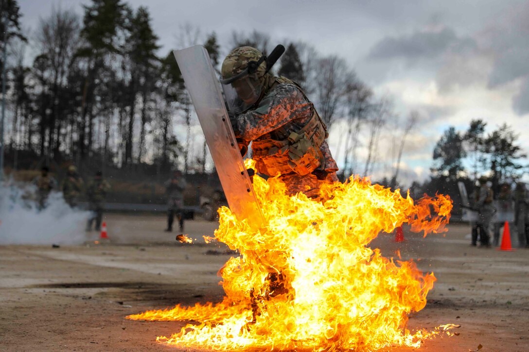 A soldier holding a shield moves through flames.