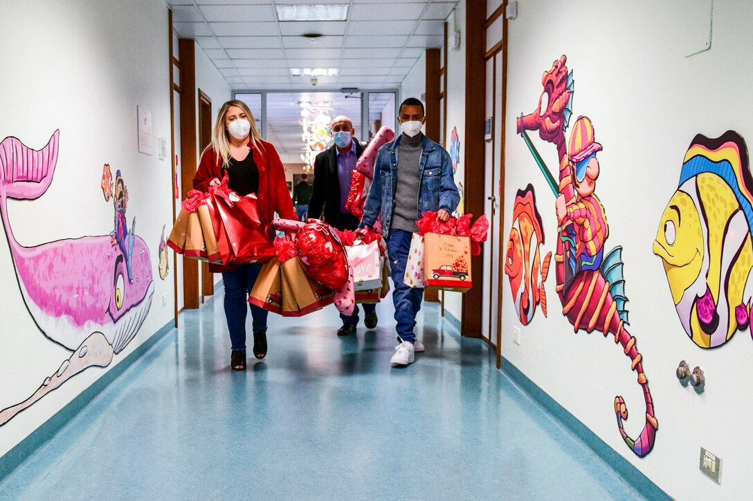 Air Force personnel in civilian clothing carry gift bags down a hall decorated with painted fish on the walls.