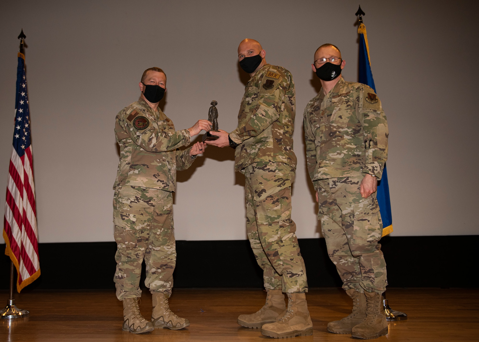 Three Airmen pose for a photo with a trophy.