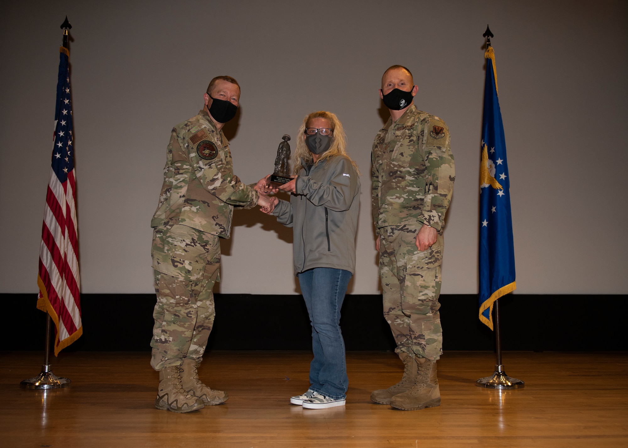 Two Airmen and a civilian pose for a photo with a trophy.