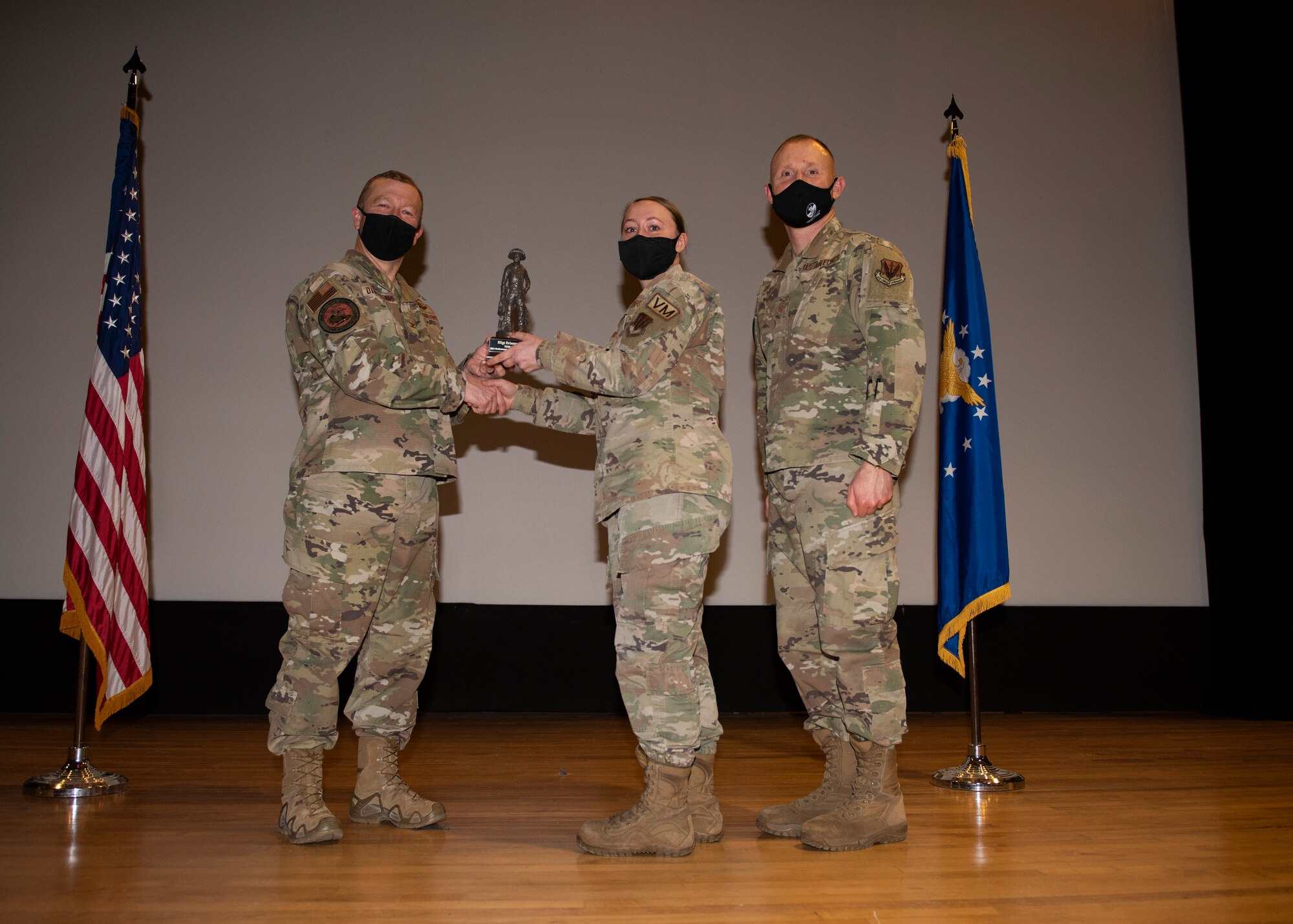 Three Airmen pose for a photo with a trophy.