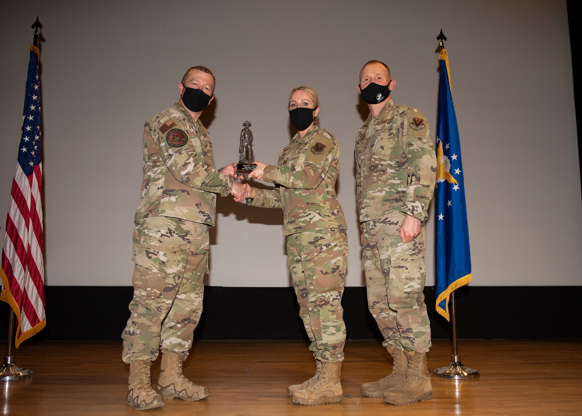Three Airmen pose for a photo with a trophy.