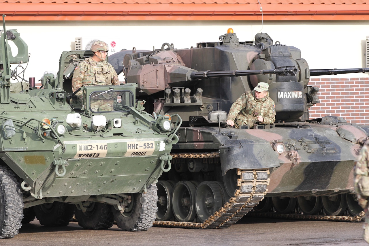 A U.S. soldier in a parked tank talks to a foreign soldier in an adjacent tank.