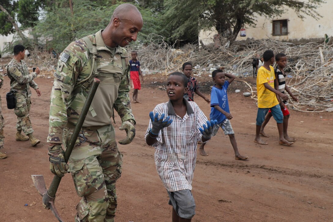 A soldier walks on a dirt road with a group of children.
