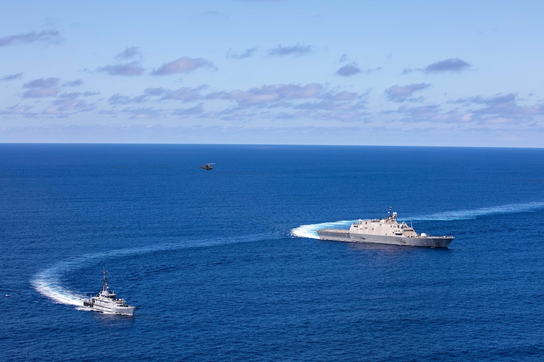 Two ships sail in the ocean while a helicopter flies above them.