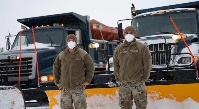 Men stand in front of snow plow.