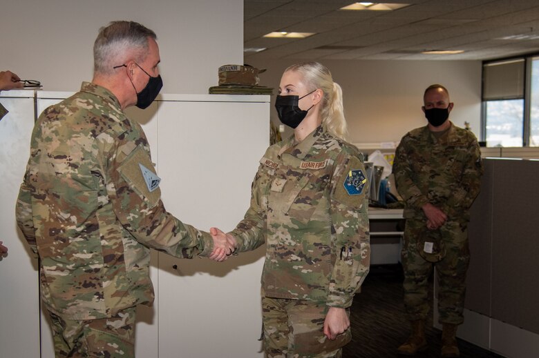 A Female Airman shakes hands with General whiting after being coined