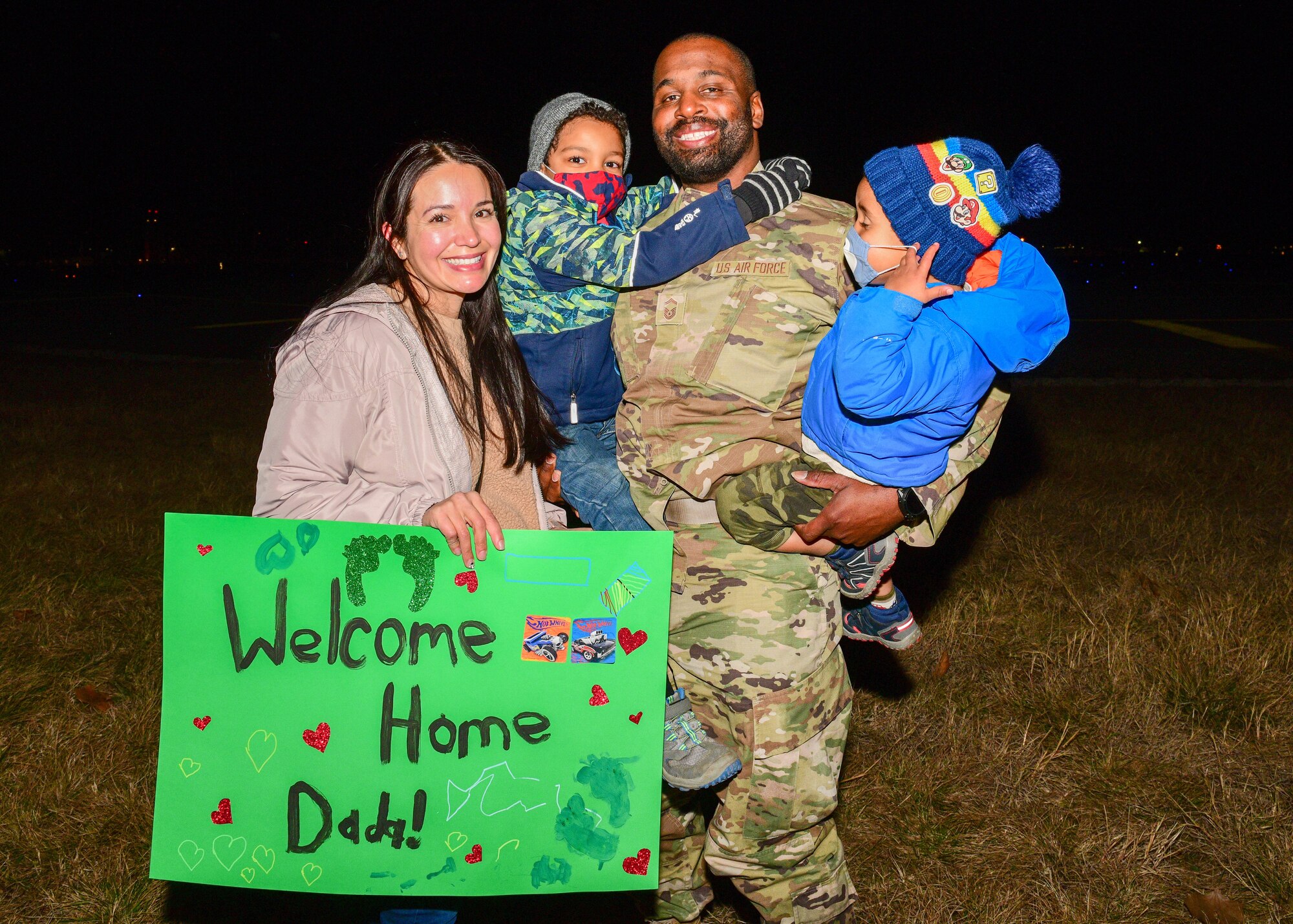 A U.S. Air Force Airman assigned to the 56th Rescue Squadron poses for a photo with his family after returning from a deployment, at Aviano Air Base, Italy, Feb. 9, 2022. Airmen with the 56th RQS and 56th Helicopter Maintenance Unit received a warm welcome from families, friends and coworkers after returning from their deployment. (U.S. Air Force photo by Senior Airman Brooke Moeder)