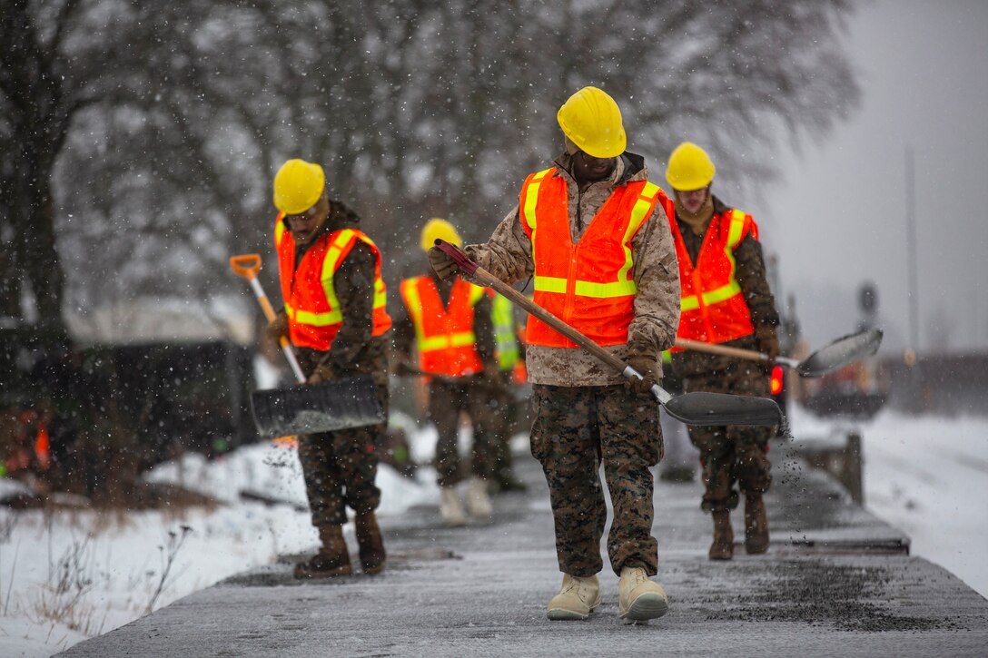 Marines carrying shovels walk through the snow.